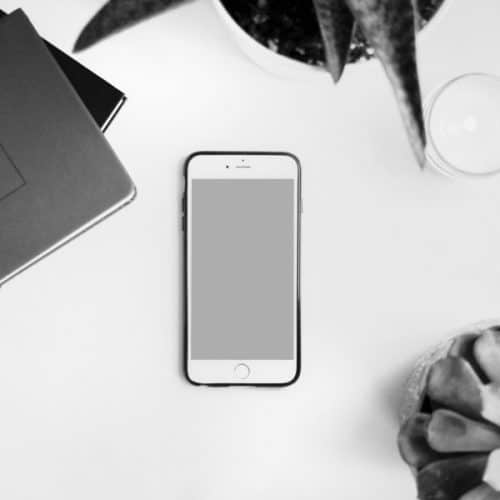 cell phone on a desk with a plant, candle, and notebooks