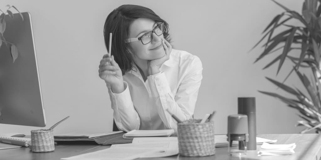 woman with a slight smile on her face, sitting at a desk looking off to the right as if daydreaming