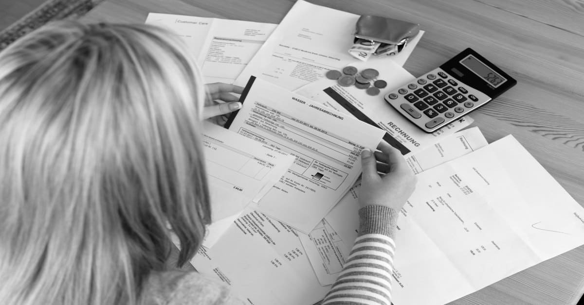 woman looking at a pile of bills with a calculator and cash money at her side