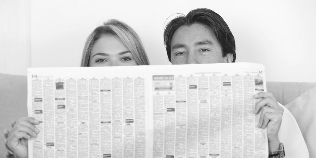 man and woman hiding lower half of face behind newspaper