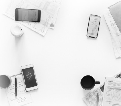 white desktop with three cell phones and various papers strewn across it