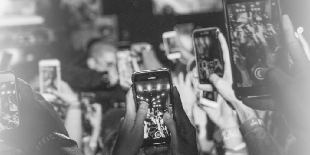 black and white photo of numerous cell phones being held in the air