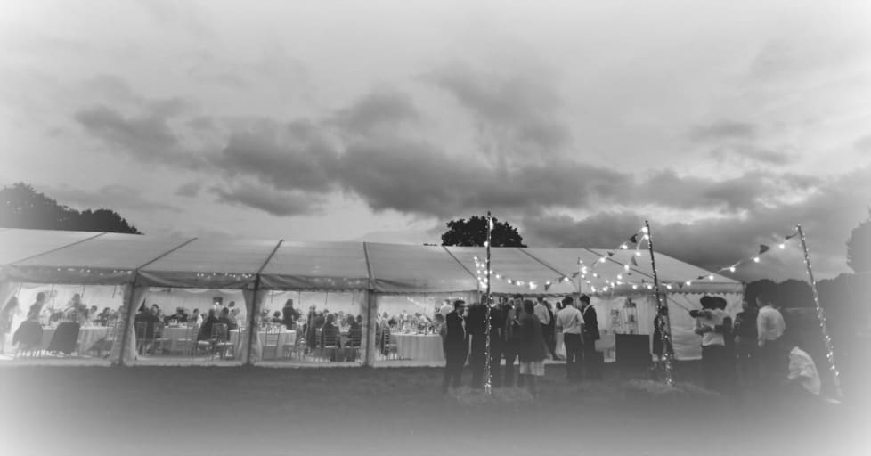 black and white image of an outdoor wedding reception under a large tent