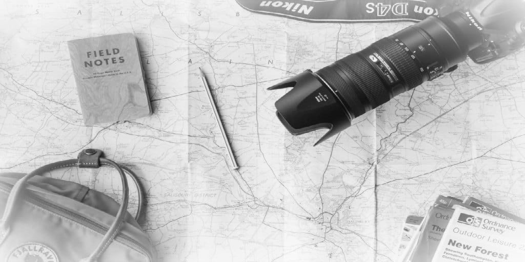 black and white photo of a map, camera, brochures, and other travel related items