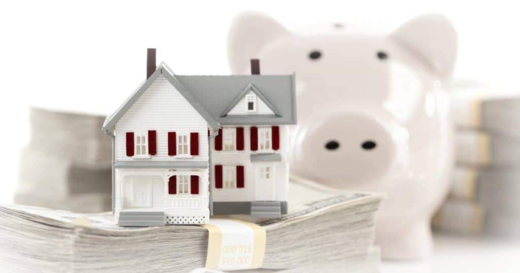 Small House and Piggy Bank with Stacks of Hundred Dollar Bills Isolated on a White Background.