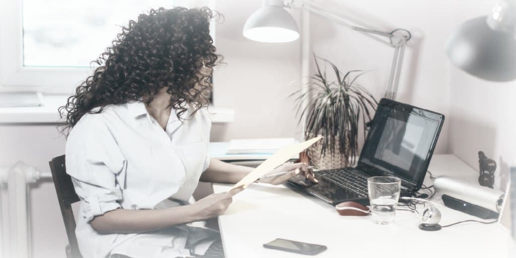 women working at a home office desk with a laptop and desk lamp on