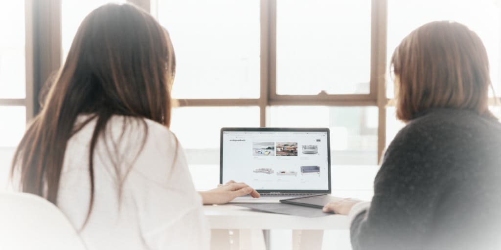 two women looking at a laptop computer sitting on a table discussing starting a business