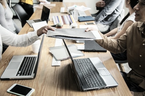 two people tugging on opposites of a work folder, sitting around a work table