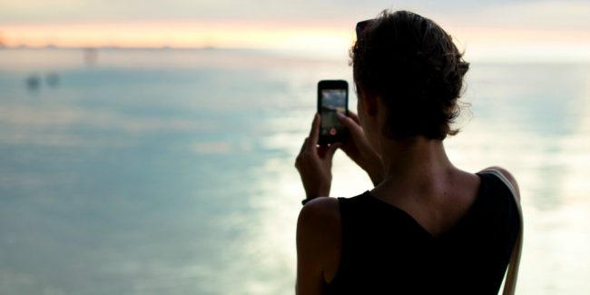 women holding a cell phone looking over water