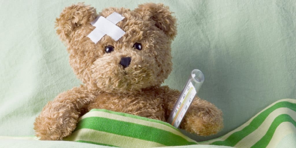 sick teddy bear in bed with a thermometer under his arm