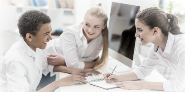 three teenages leaning on a desk discussing work