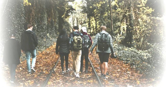 teenagers walking down railroad tracks wearing school backpacks