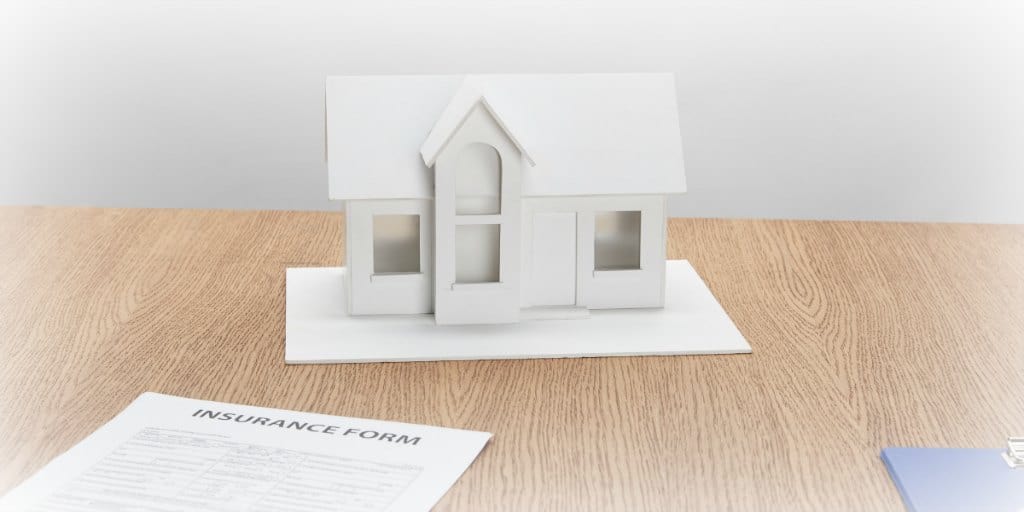 white model of a home and an insurance form on a brown desk