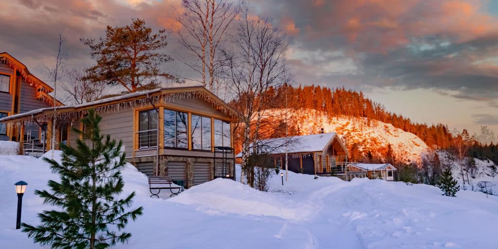 Vacation cottages with panoramic windows in the village. Wooden house on the background of the hills. Snow near suburban cottages. Country village on the of nature.