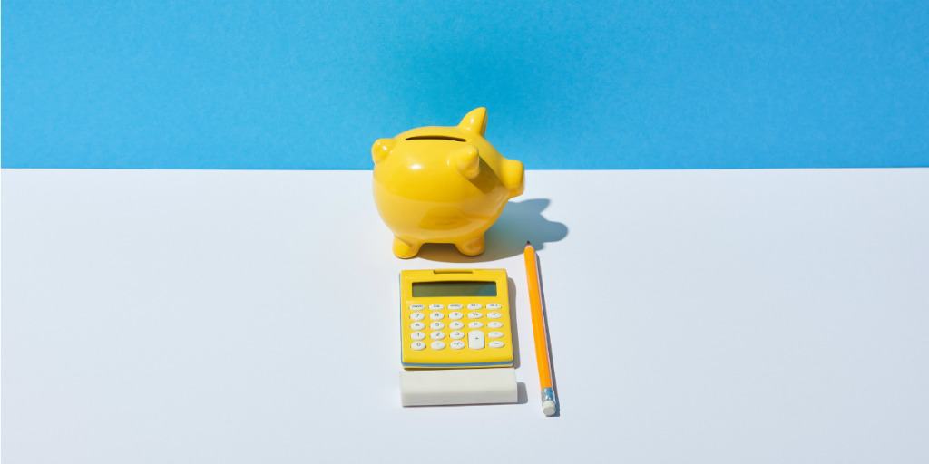 yellow piggy bank, yellow calculator, and yellow pencil on white table against a blue background