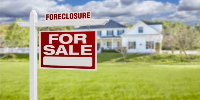 red foreclosure for sale sign in front of a white home