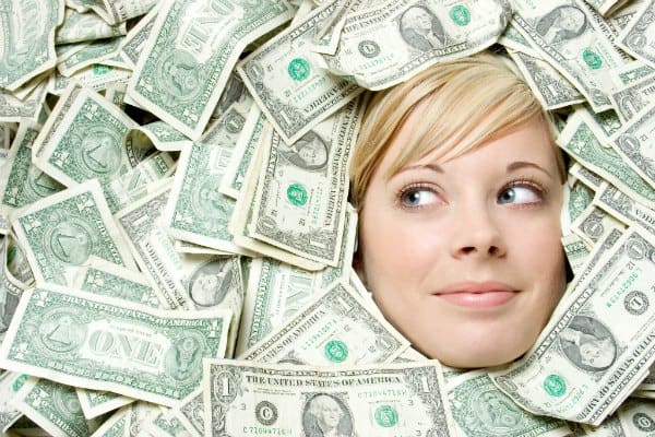 female face peaking out from under a pile of dollar bills