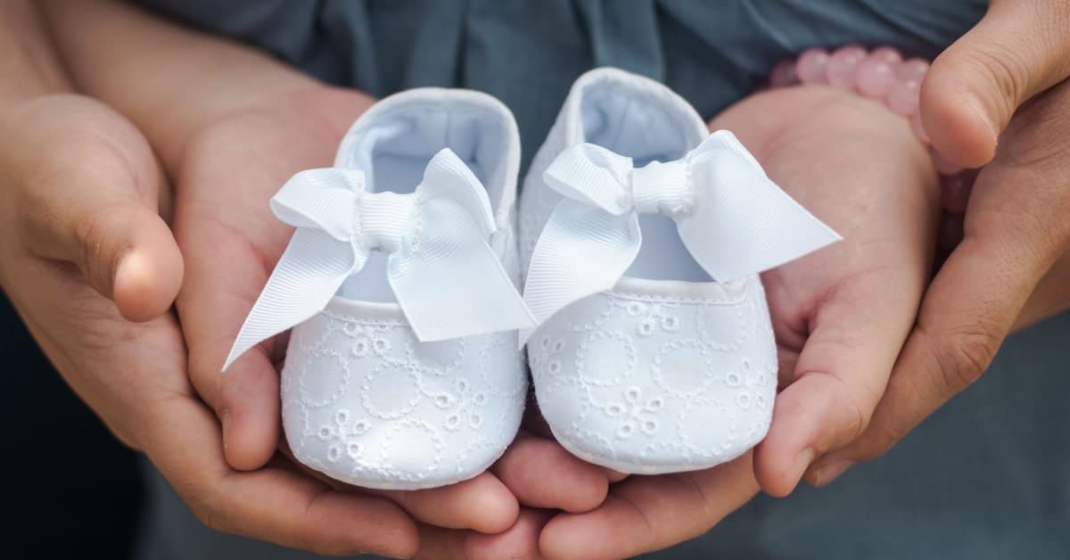 dainty white baby shoes held in hands of expectant parents