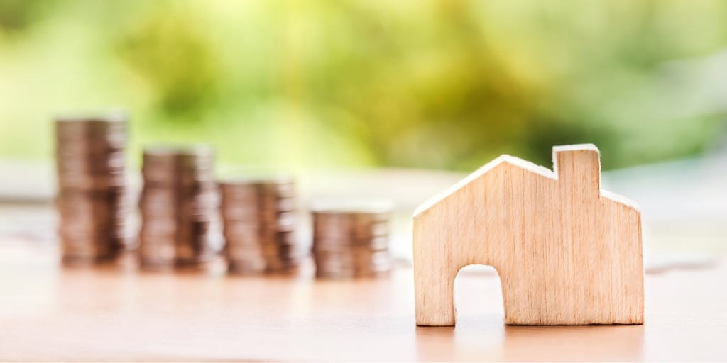 saving for first house depicted with stacks of coins and a model house