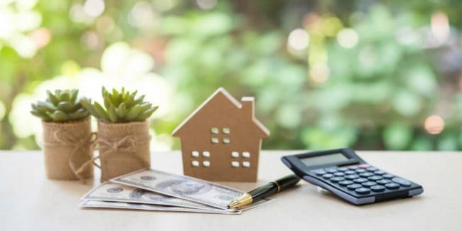 graphic of money on a desk with a pen, a calculator, and a small model house representing a cash out refinance