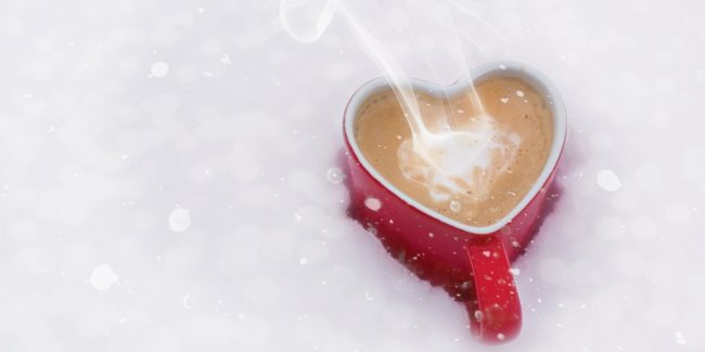 heart shaped red mug full of hot chocolate sitting in snow