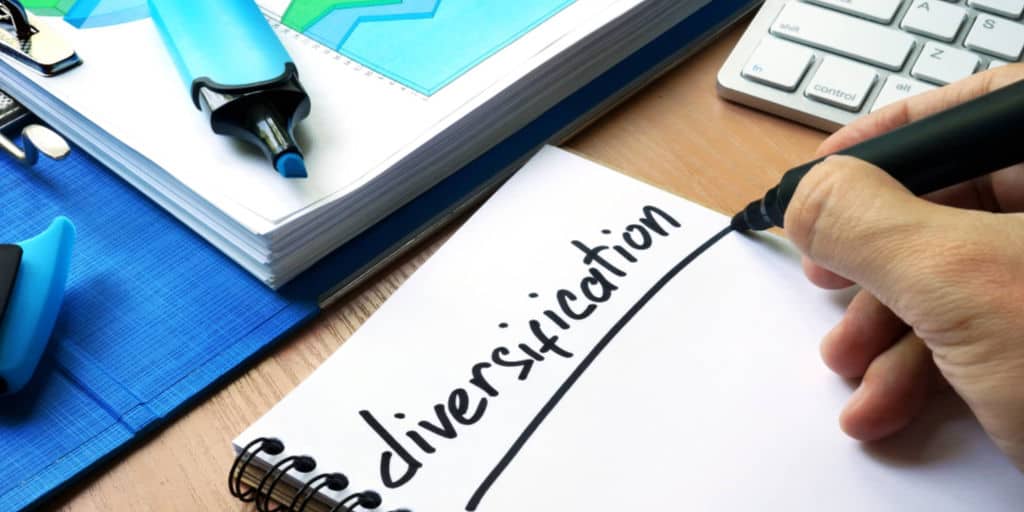 person writing the word diversification in notebook with black felt marker