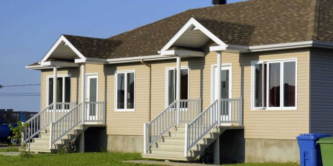 duplex home with tan siding, white trim, and a brown roof