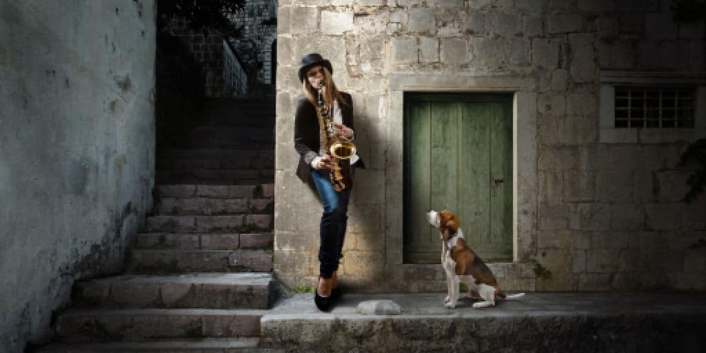 female playing the blues on her saxophone with her dog watching