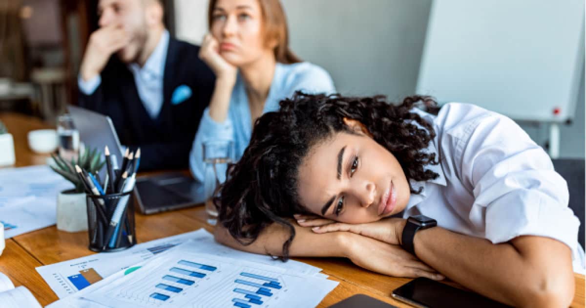 unhappy woman in office meeting with head on hands while colleague stares off in space