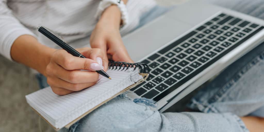 woman taking notes during online learning