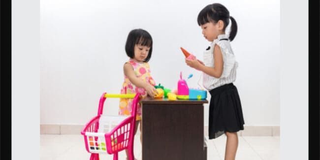 Asian Chinese little sisters pretending as customer and cashier with toy shopping cart and cash register