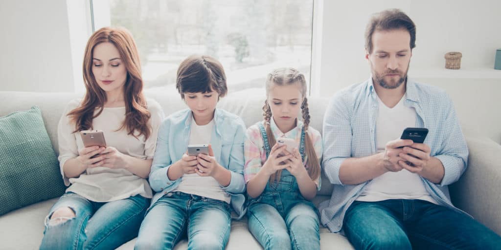 two parents and two kids sitting on couch and looking at their smart phone money apps