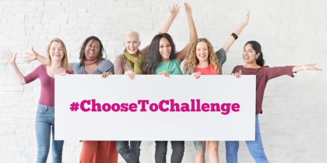 group of women holding a sign that reads choose to challenge and raising arms in celebration