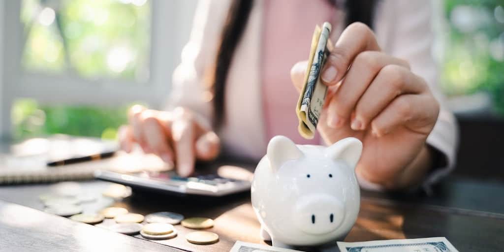 Closeup of woman hand putting money into piggy bank for saving money. saving money and budgeting concept