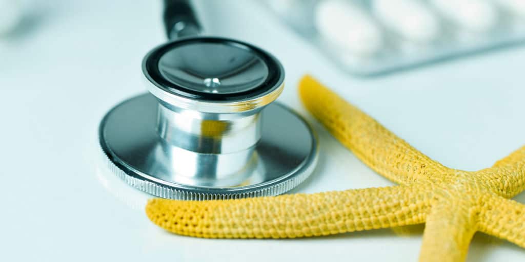 closeup of a yellow starfish on a doctors office, next to a computer keyboard, a stethoscope and some pills, depicting the medical aid during summer travel concept