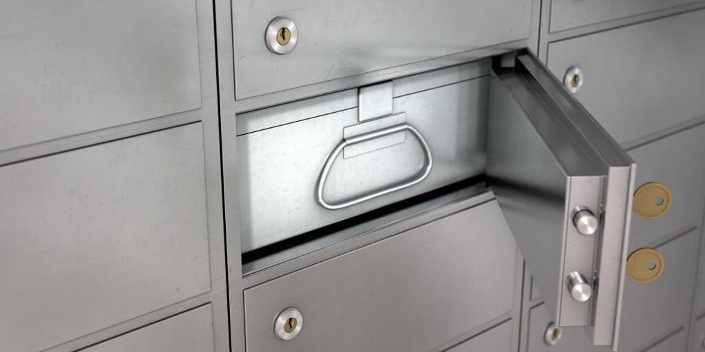 A closeup of a wall of closed metal safety deposit boxes with one open revealing its contents inside