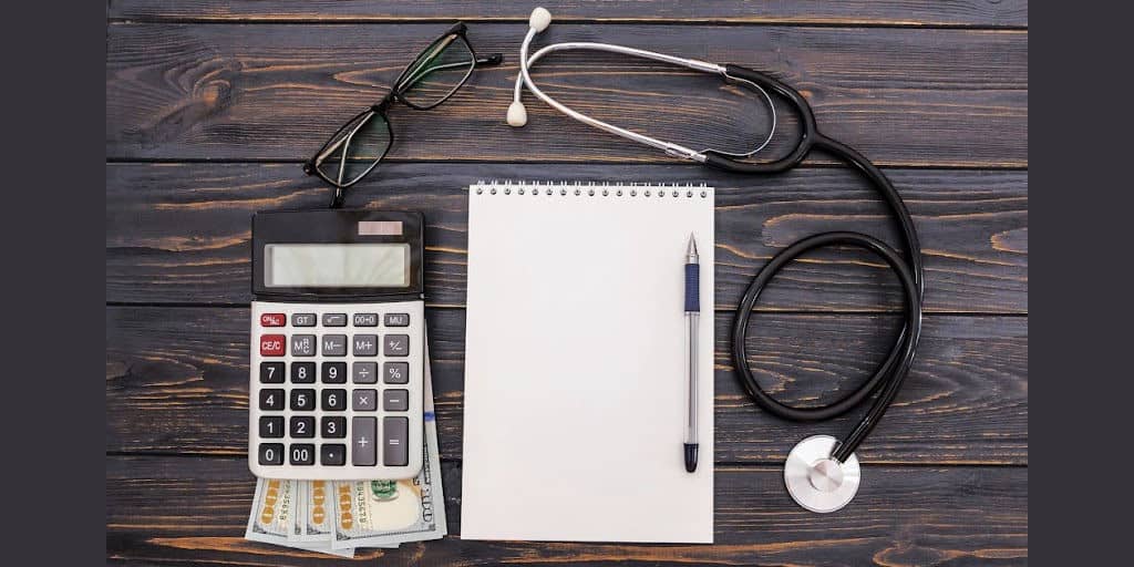 calculator, cash, stethoscope, and notepad on desktop symbolizing saving money for healthcare in a medical savings account