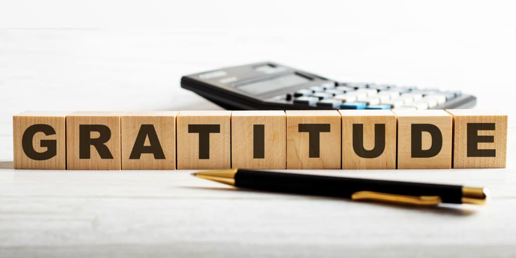 wooden tile letters spelling gratitude with calculator in background and pen in foreground 