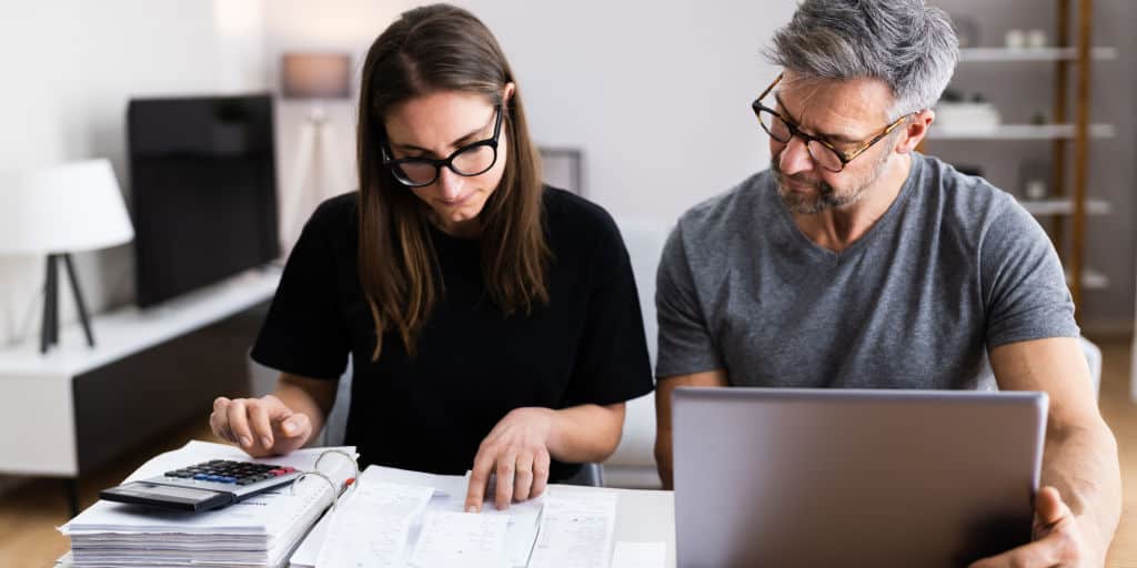 heterosexual couple reviewing financials using calculator and computer