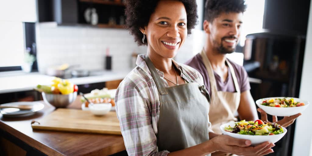 african american couple holding a meal they made in individual serving bowls