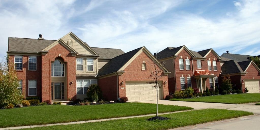 two large brick dream homes in subdivision setting with green grass lawn and blue sky