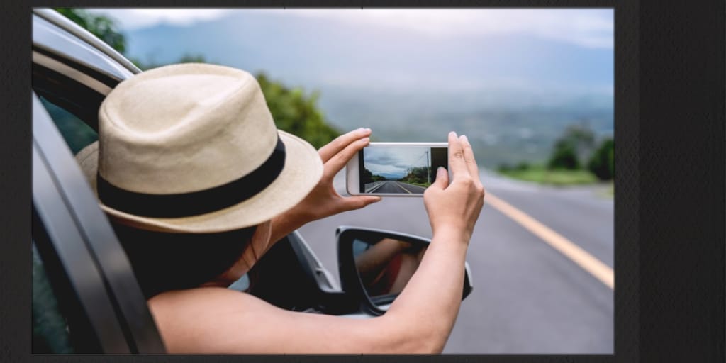 woman leaning out of car during road trip to take a photo on her smartphone