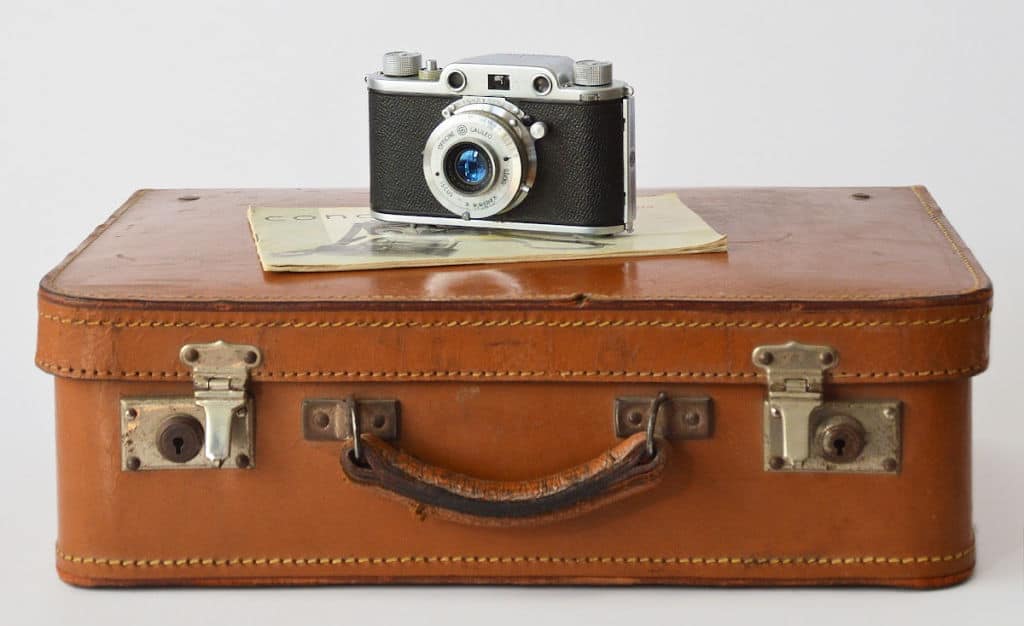 camera sitting on top of closed brown suitcase