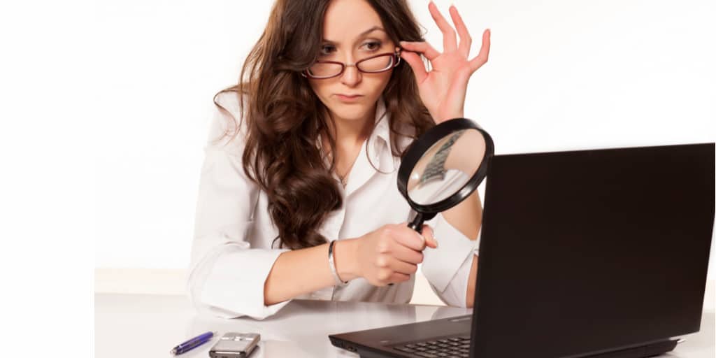 woman with magnifying glass looking at laptop in act of investigating