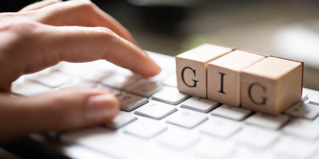 close up of female hand on white keyboard with wooden block letters that spell gig