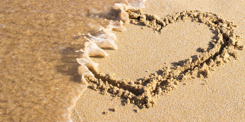 heart drawn in sand being washed away by water coming in from tide