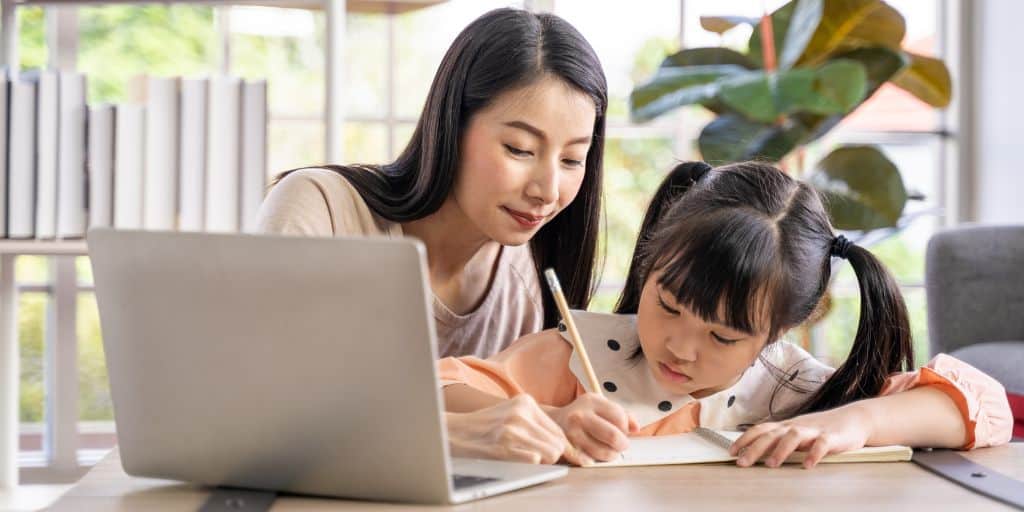 young girl writing on paper with pencil as mom teaches