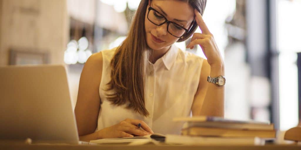 woman reading books and studying at desk with laptop