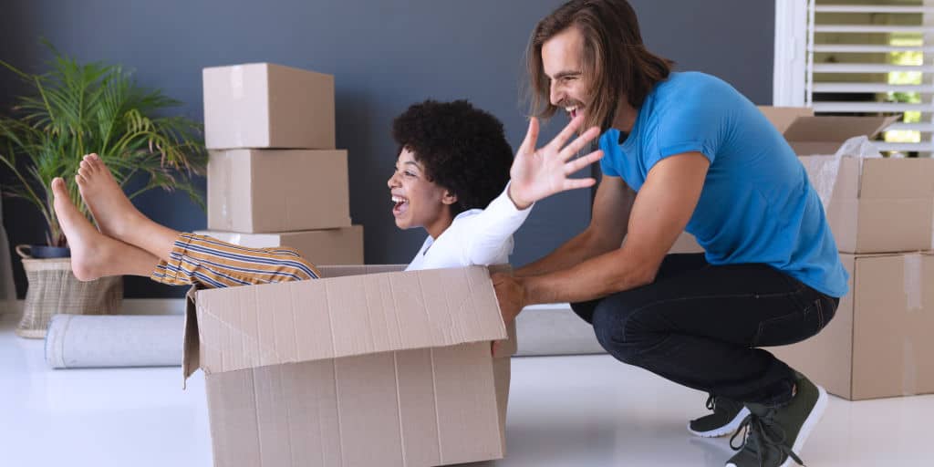 young female inside large moving box being pushed by young male in fun