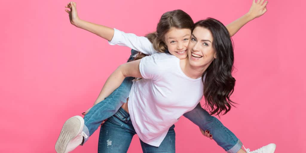 young mom giving daughter a piggy back ride on her back